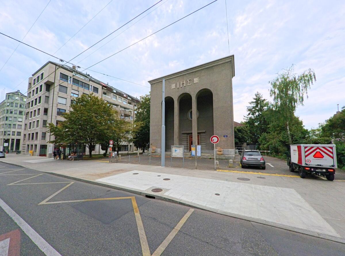 Eine Kirche mit schlichten Säulen steht in Genève (1203, Kanton Genf) an einer ruhigen Strasse neben modernen Gebäuden und Bäumen.
