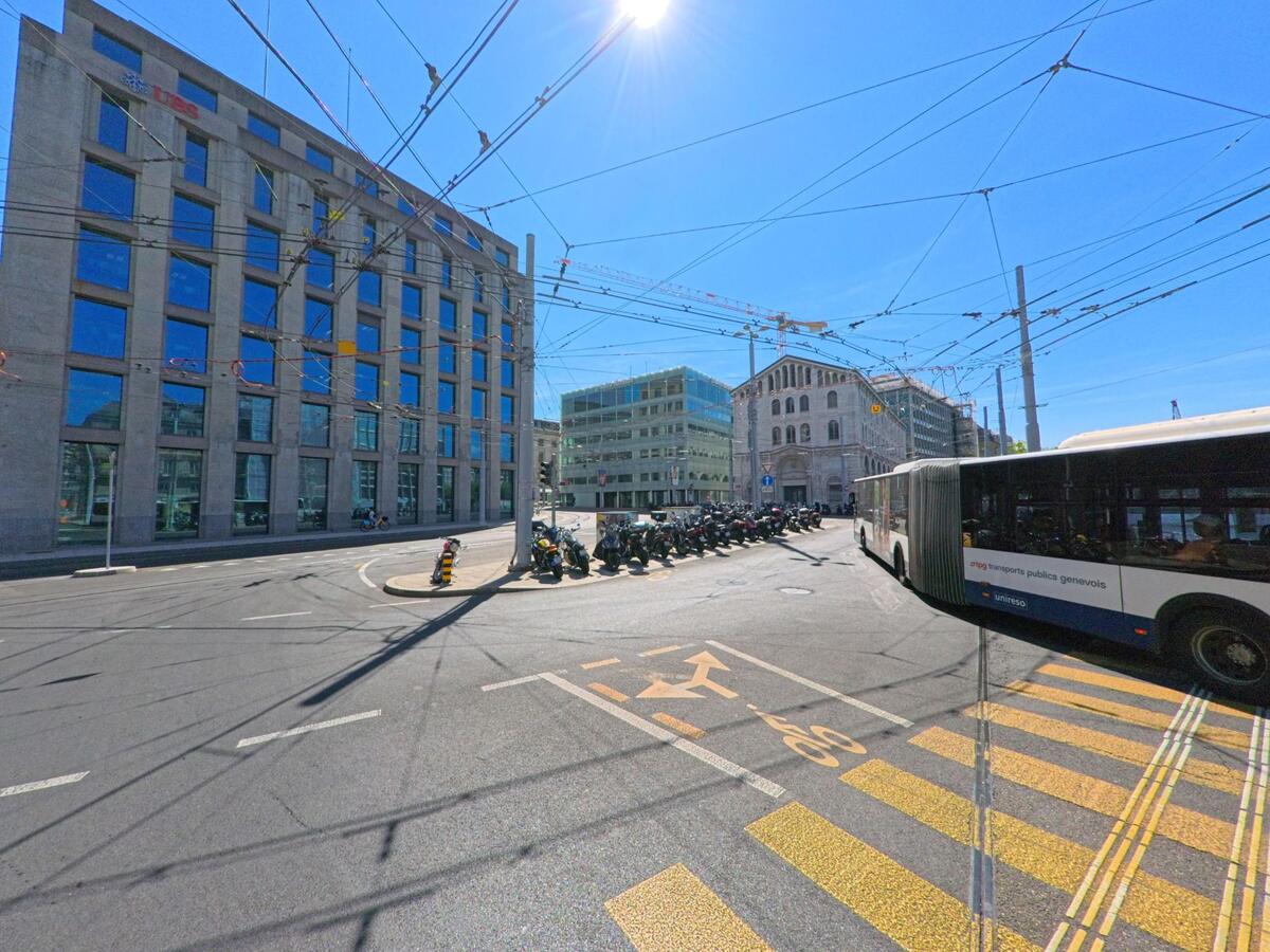 In Genève (1204, Kanton Genf) kreuzen sich Buslinien und Oberleitungen an einer grossen Kreuzung zwischen modernen Gebäuden und der UBS-Fassade.
