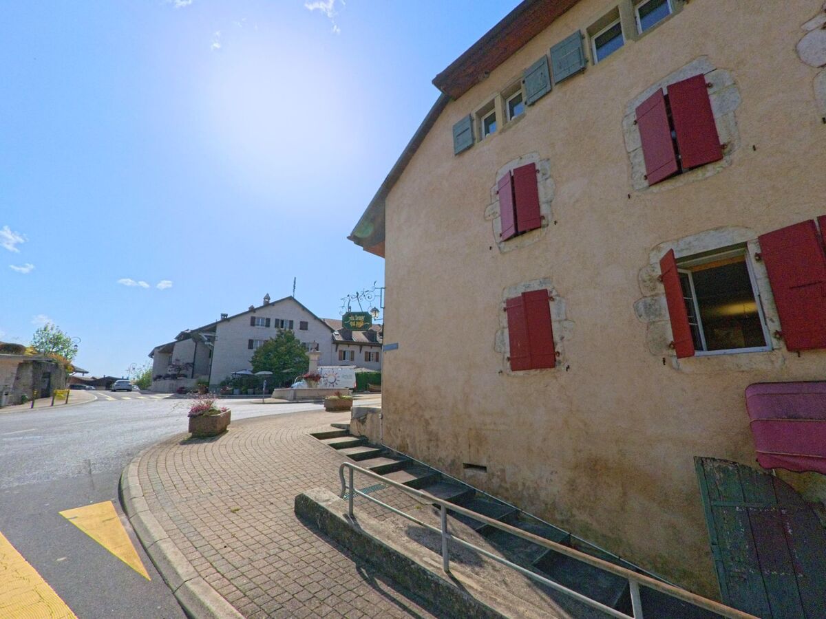 In Genolier (1272, Kanton Waadt) fuehrt eine gepflasterte Strasse mit leichten Steigungen vorbei an alten Haeusern mit roten Fensterlaeden.