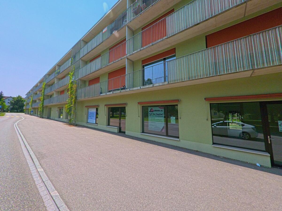 In Gerlafingen (4563, Kanton Solothurn) verläuft eine geschwungene Strasse entlang eines modernen Wohn- und Geschäftsgebäudes mit grossen Balkonen und begrünten Fassadenteilen.