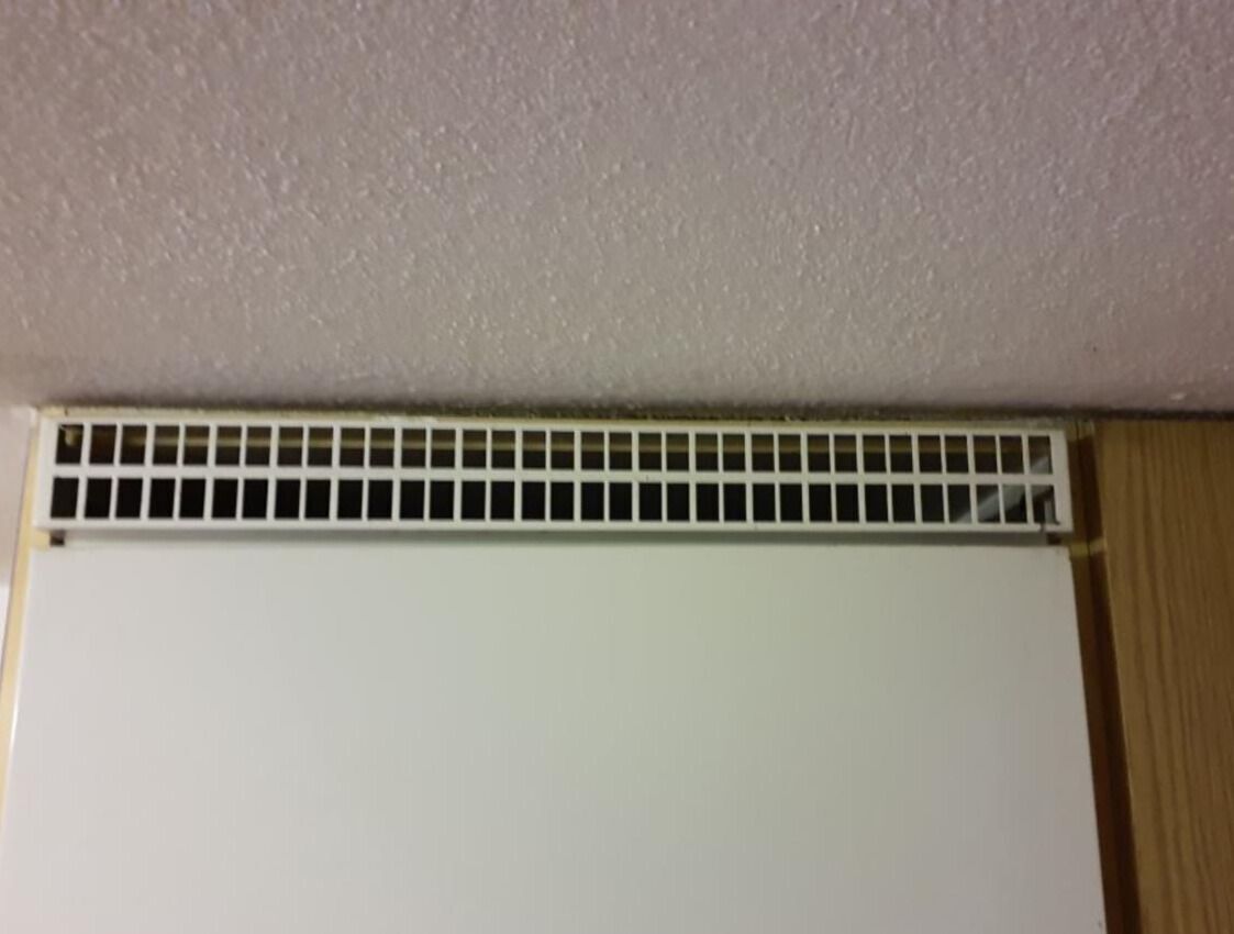 In Geroldswil (8954, Kanton Zürich) ist der Blick auf ein Heizgitter zu sehen, das an der Wand angebracht ist und eine weisse Wand darunter freigibt.