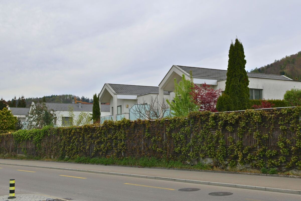 In Geroldswil im Kanton Zürich mit der PLZ 8954 stehen moderne Einfamilienhäuser hinter einer bewachsenen Mauer am Strassenrand.