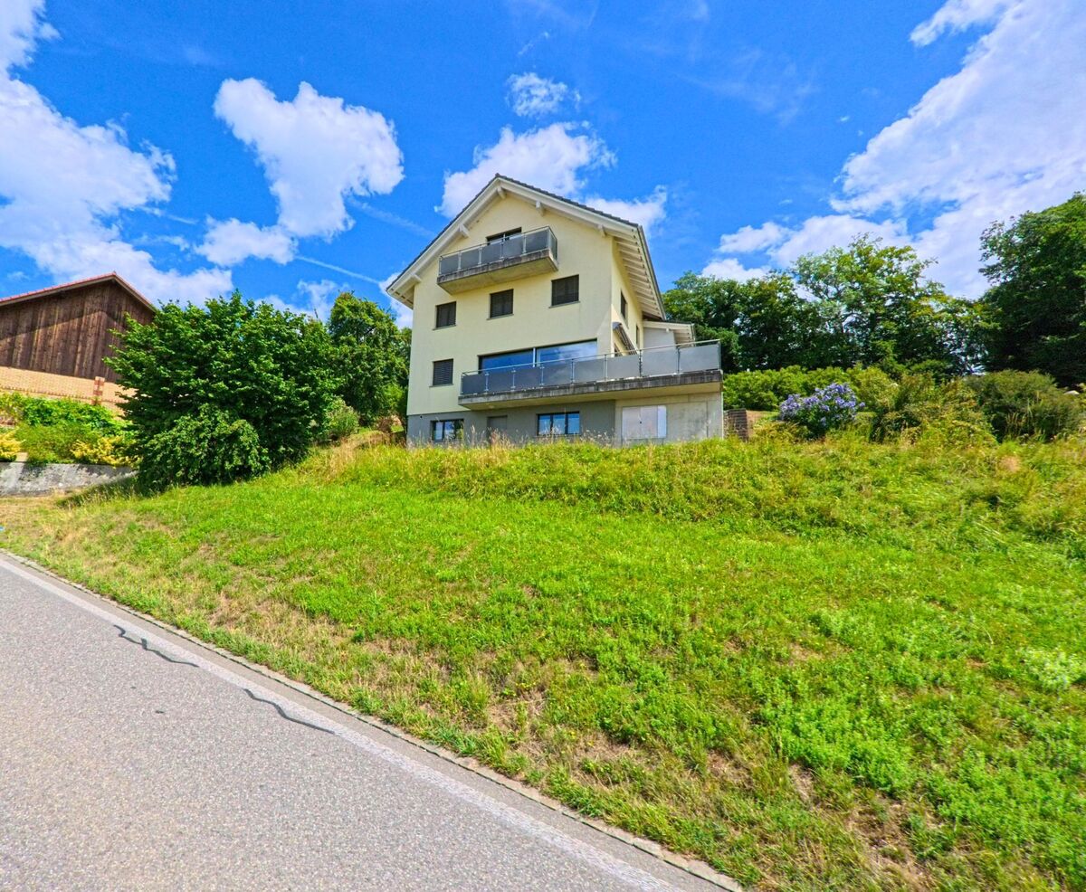Am Hang von Geuensee (6232, Kanton Luzern) steht ein Einfamilienhaus mit Balkonen, umgeben von gruener Wiese und nahegelegenen Baeumen.