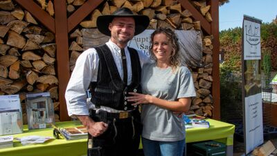 In Wiesendangen (8542, Kanton Zuerich) stehen zwei Mitglieder des Gewerbevereins vor einem Holzstapel an einem Infostand und laecheln in die Kamera.