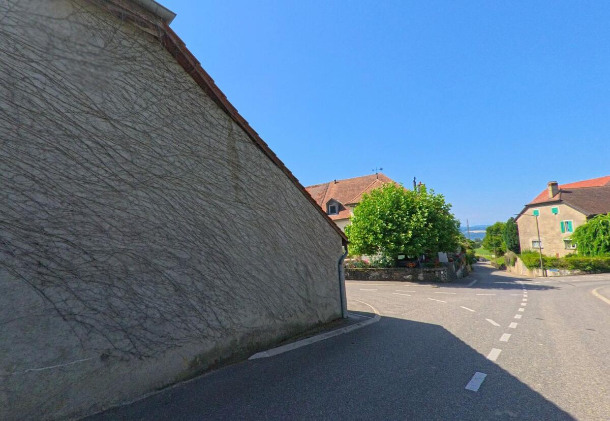 Eine enge Strasse in Giez (1429, Kanton Waadt) führt zwischen Häusern mit roten Ziegeldächern hindurch, am Ende ist ein Baum am Strassenrand sichtbar.