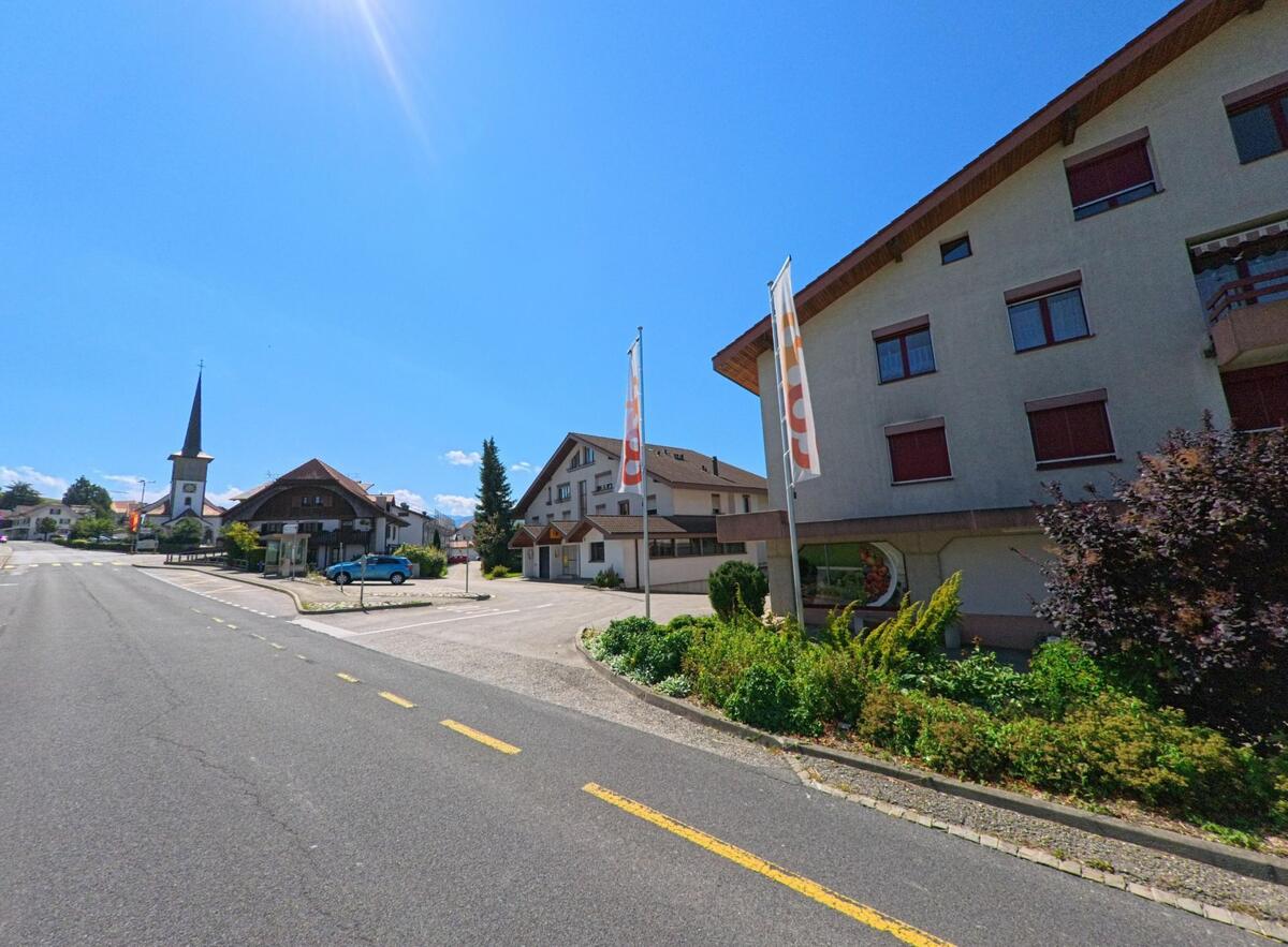 Von der Hauptstrasse in Giffers (1735, Kanton Freiburg) fällt der Blick auf die Kirche mit spitzem Turm und umliegende Wohn- und Geschäftshäuser.