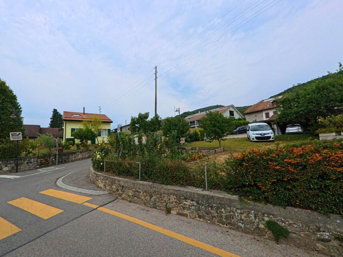 Am Ortseingang von Gilly (1182, Kanton Waadt) stehen Einfamilienhaeuser mit gepflegten Gaerten und angrenzenden Strassen.