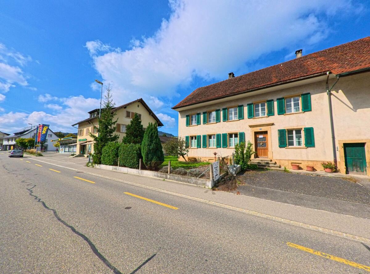 Entlang der Hauptstrasse in Gipf-Oberfrick (5073, Kanton Aargau) stehen gepflegte Wohnhaeuser mit grünen Fensterlaeden und kleinen Gaerten unter blauem Himmel.