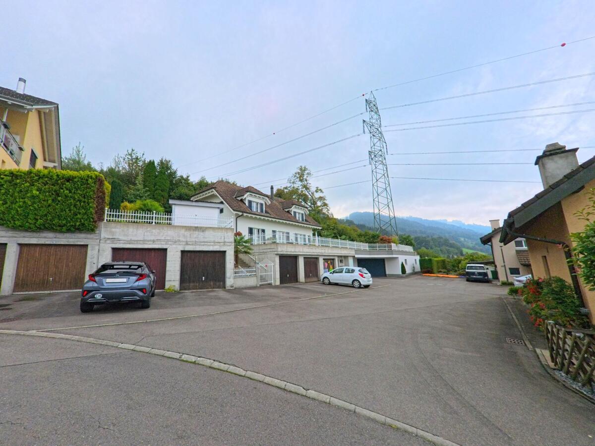 In einem ruhigen Wohngebiet von Gisikon (6038, Kanton Luzern) stehen Einfamilienhaeuser mit Garagenplaetzen und Strommast im Hintergrund.