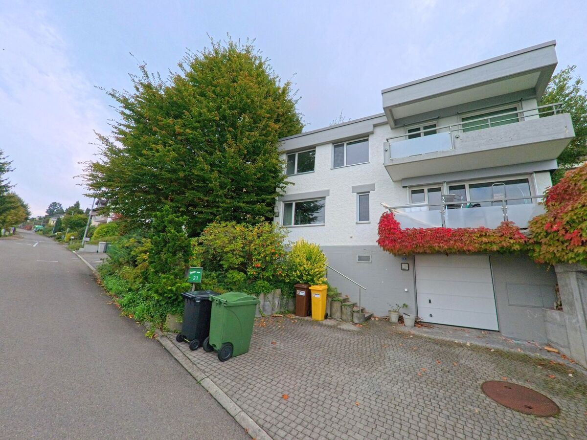 Ein modernes Wohnhaus in Gisikon (6038, Kanton Luzern) mit Balkon und herbstlich bewachsenen Fassaden steht an einer ruhigen Anwohnerstrasse.
