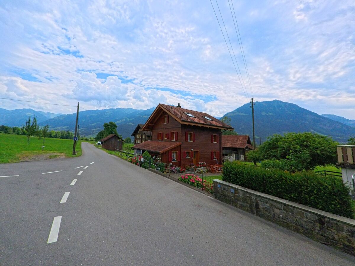 Ein traditionelles Wohnhaus mit roten Fensterlaeden steht in Giswil (6074, Kanton Obwalden) an einer ruhigen Nebenstrasse mit Blick auf die umliegenden Berge.