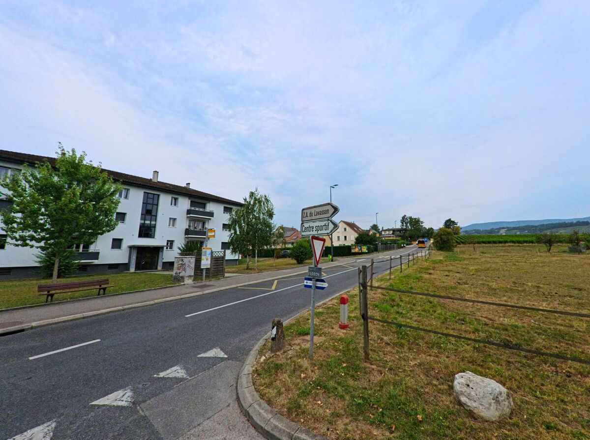 Ein Strassenschild weist in Gland (1196, Kanton Waadt) den Weg zum Sportzentrum, daneben stehen Wohnhaeuser und Felder.