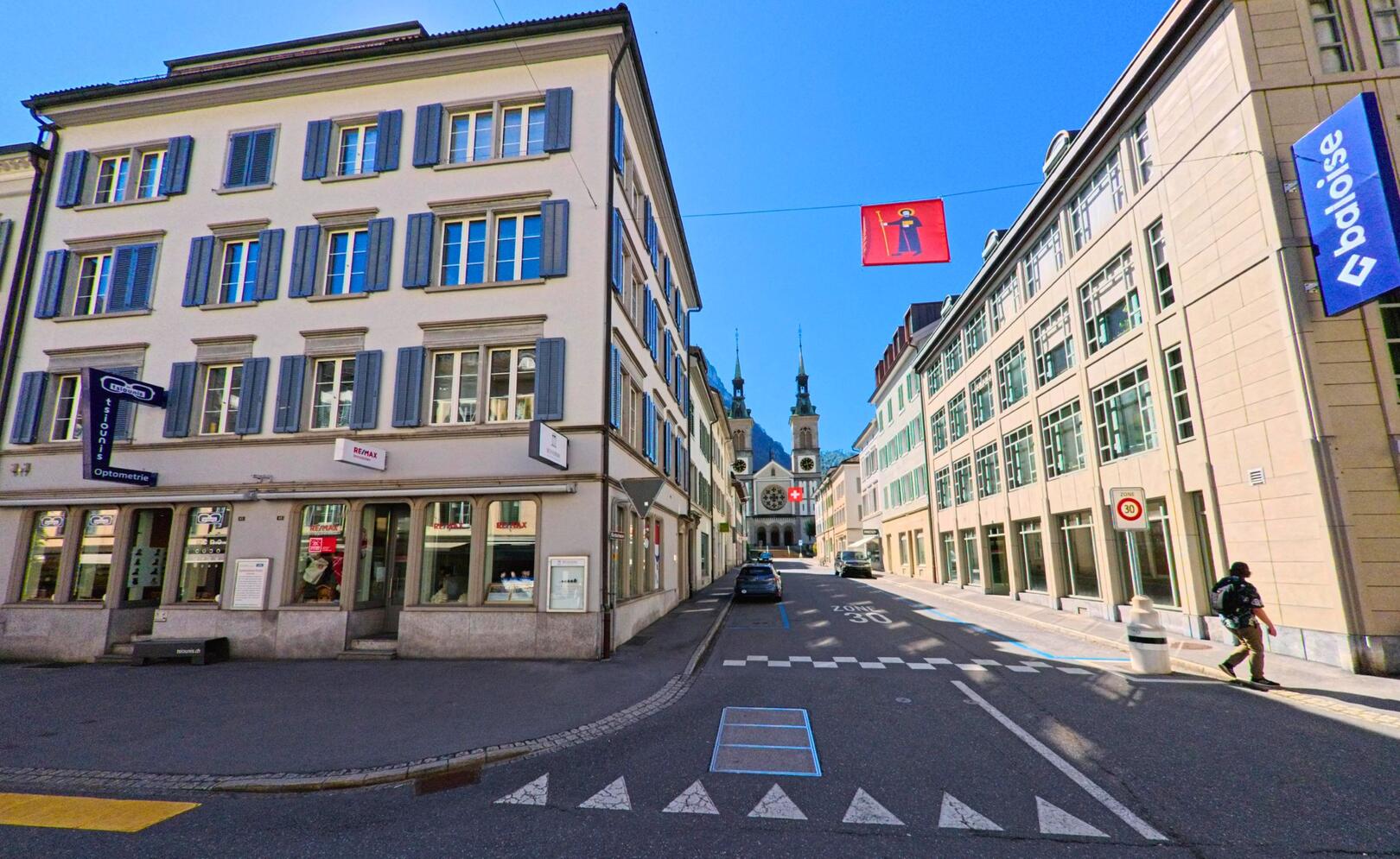 Zwischen gepflegten Stadthaeusern in Glarus (8750, Kanton Glarus) fuehrt eine schmale Strasse mit Blick auf die Kirche im Hintergrund durch das Zentrum.