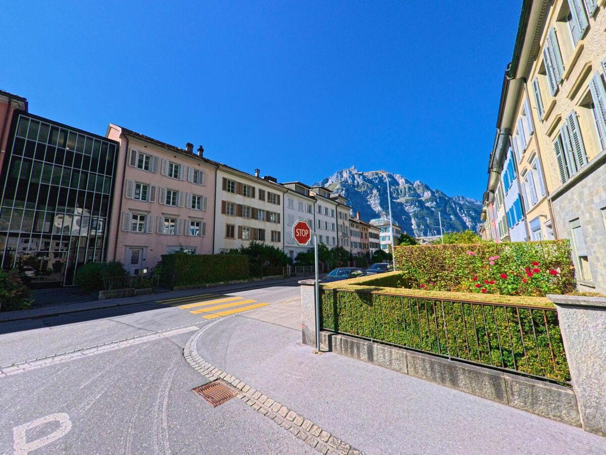 In Glarus (8750, Kanton Glarus) fuehrt eine ruhige Strasse mit gepflegten Stadthaeusern und Blick auf den imposanten Berg ins Wohnquartier.