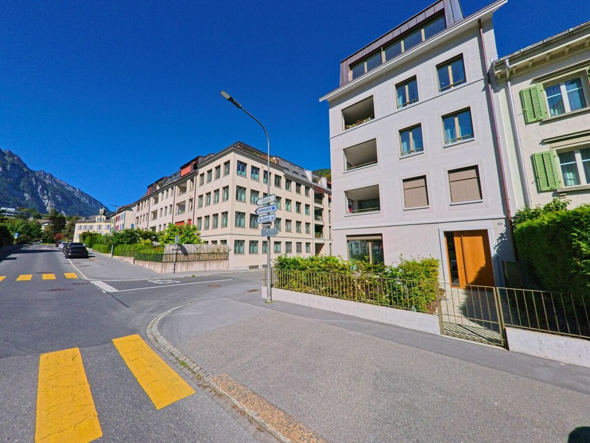 Mehrfamilienhaeuser in Glarus (8755, Kanton Glarus) stehen an einer ruhigen Strasse mit Fussgaengerstreifen und Blick auf die umliegenden Berge.