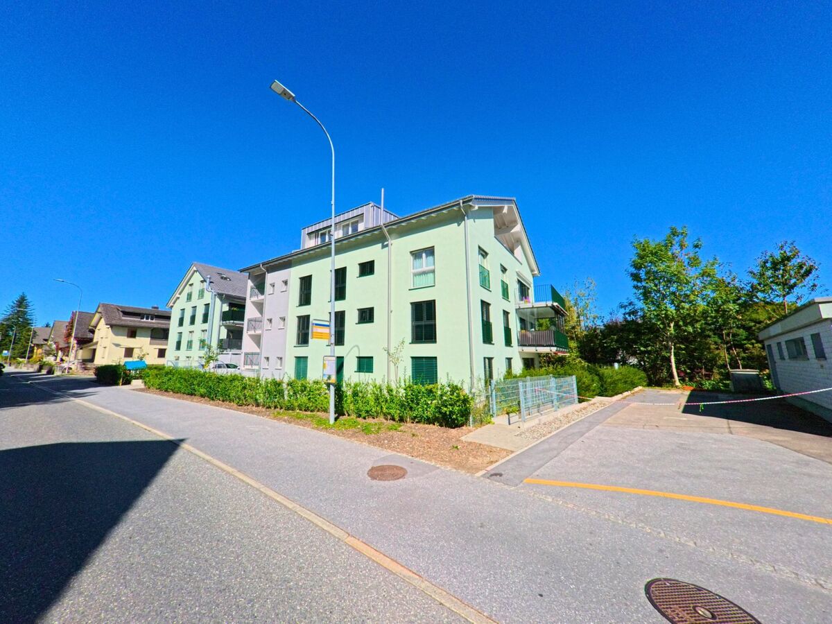 An einer ruhigen Wohnstrasse steht ein hellgrünes Mehrfamilienhaus mit Balkonen in Glarus Nord (8865, Kanton Glarus), umgeben von Gehwegen, Bepflanzung und benachbarten Wohnbauten.