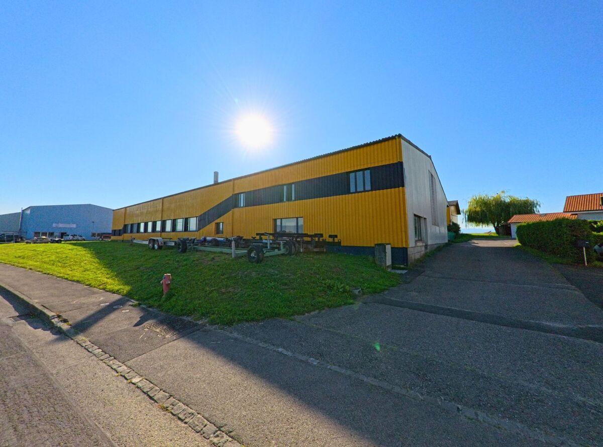 Eine gelb-schwarz gestrichene Industriehalle steht in Gletterens (1544, Kanton Freiburg) unter strahlender Sonne an einer asphaltierten Zufahrt.