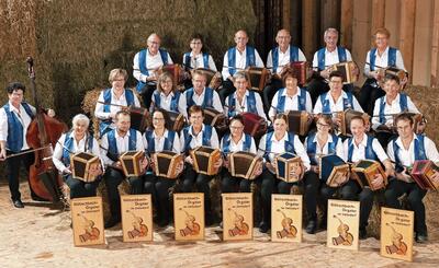 Eine grosse Gruppe von Musikerinnen und Musikern mit Handorgeln sitzt vor Heuballen in Uetendorf (3661, Kanton Bern) und zeigt traditionelle Volksmusik.