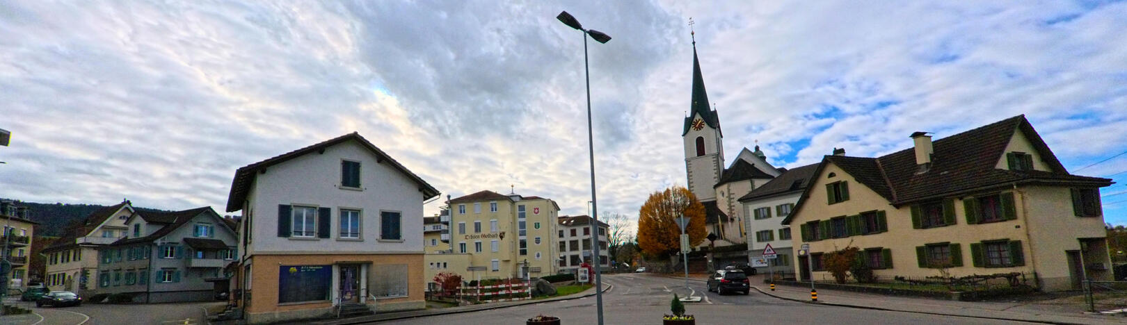 In Goldach (9403, Kanton St. Gallen) zeigt die Aufnahme einen zentralen Strassenbereich mit Wohnhaeusern und der markanten Kirche vor einer weit aufgezogenen Wolkendecke.