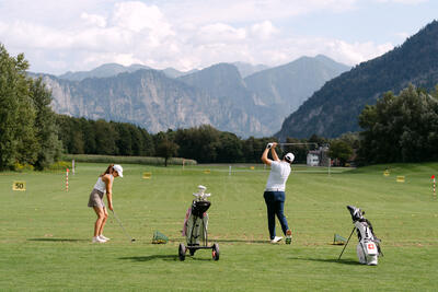 Auf der Golfuebungsanlage in Bad Ragaz (7310, Kanton St. Gallen) schlagen zwei Personen auf einer weiten Wiese Golfbaelle mit Blick auf die umliegenden Berge.