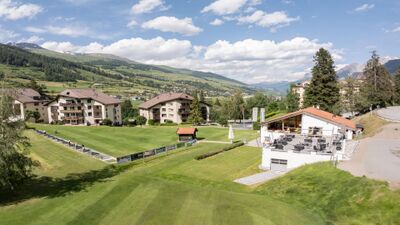 In Vulpera (7552, Kanton Graubuenden) liegt der Golf Club Vulpera mit Terrasse am Clubhaus, umgeben von gepflegtem Gruen und Blick auf die Berge.