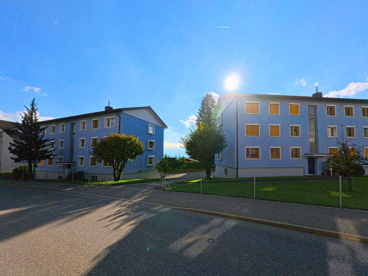 Mehrere Wohnbloecke liegen an einer ruhigen Strasse in Gommiswald (8737, Kanton St. Gallen) im Gegenlicht der Sonne.