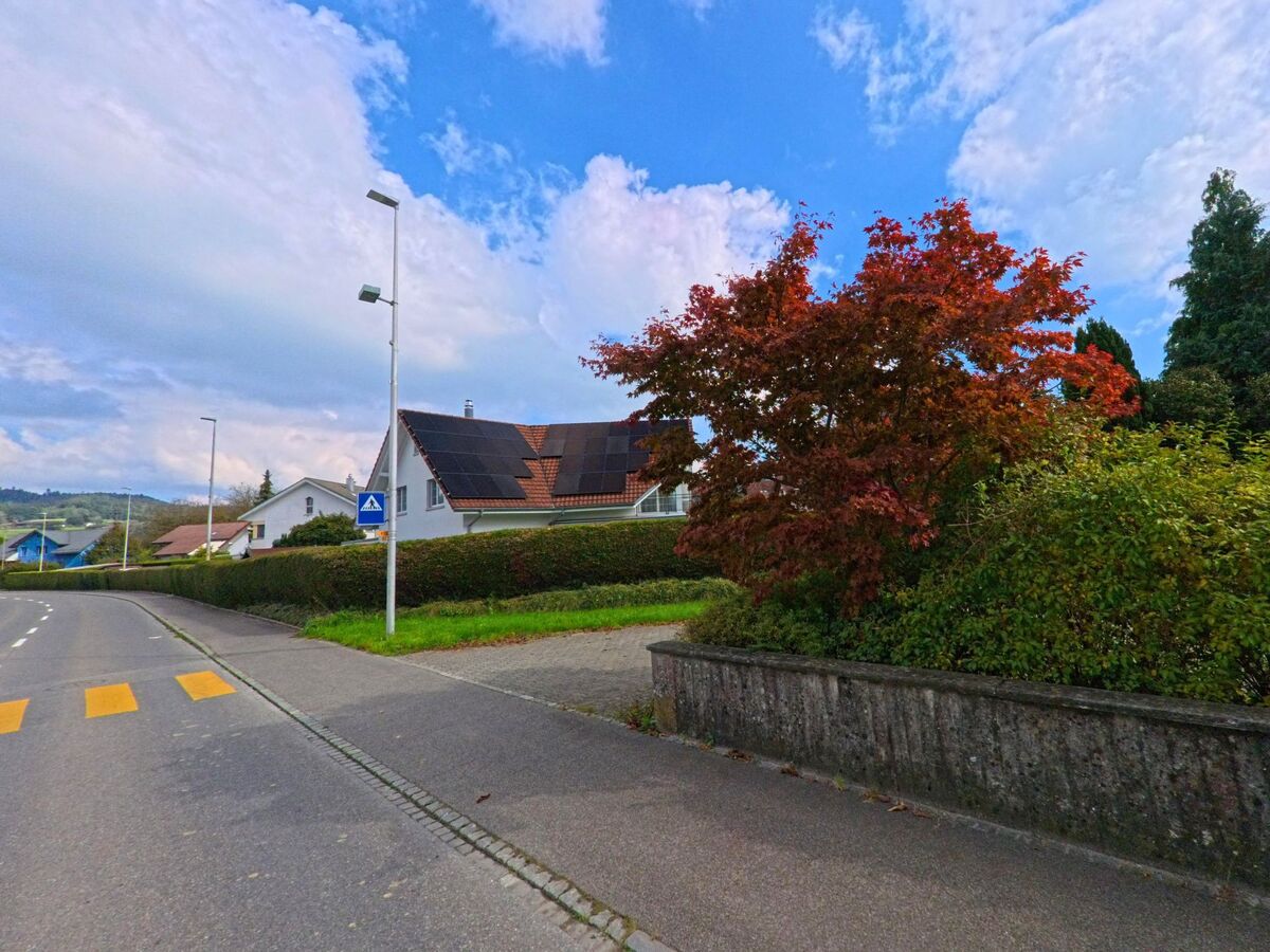 Neben einer Kreuzung mit Gehweg zeigt sich ein Wohnhaus mit herbstlichem Baum in Gonten (9108, Kanton Appenzell Innerrhoden).