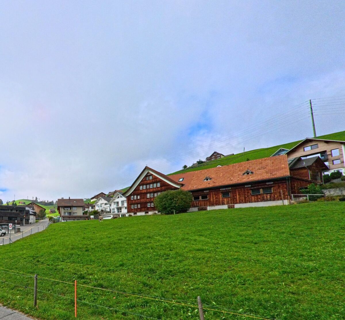 Traditionelle Gebäude mit Satteldach stehen oberhalb einer grünen Fläche in Gonten (9108, Kanton Appenzell Innerrhoden).