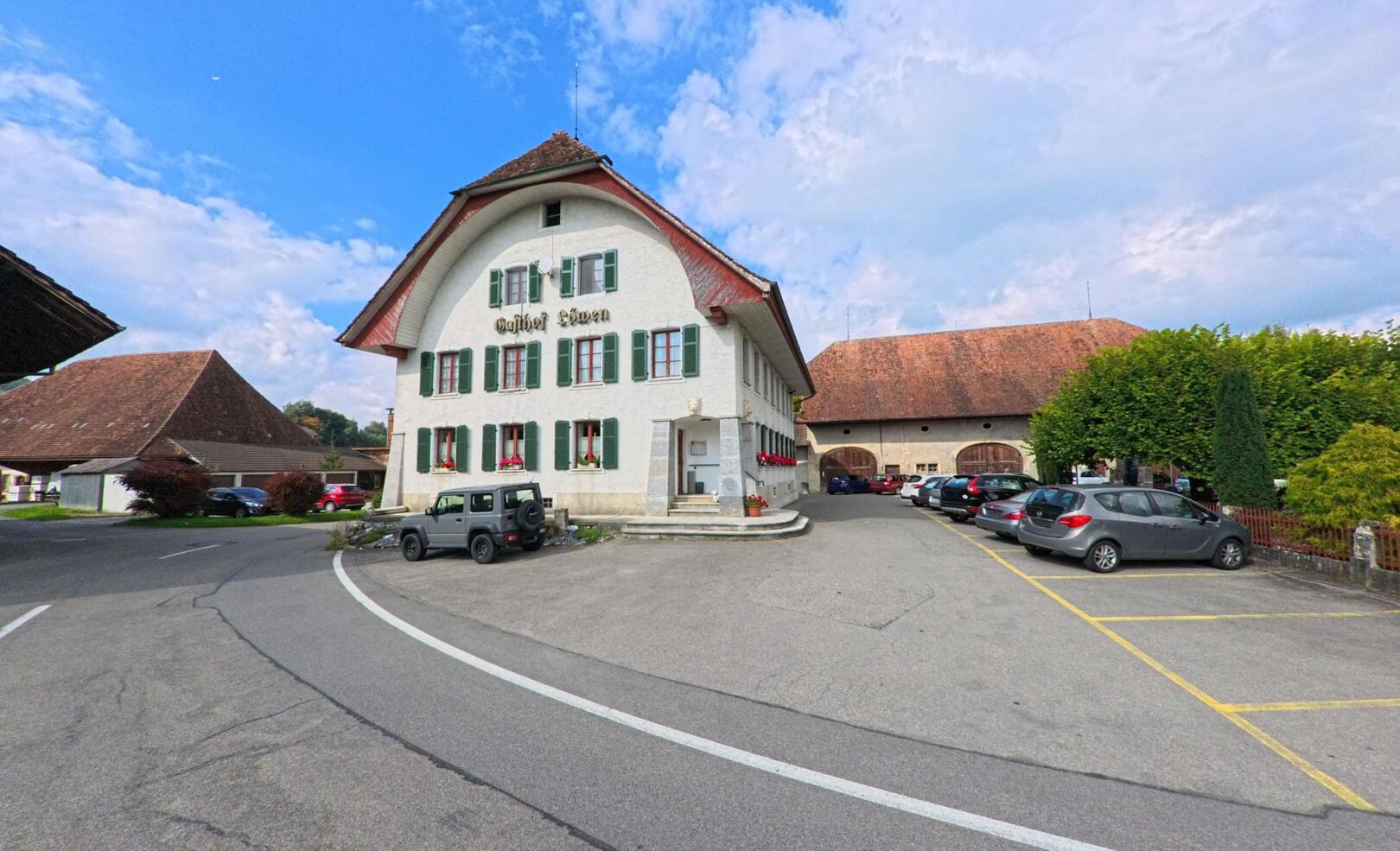 Das traditionelle Gasthaus Löwen in Gontenschwil (5728, Kanton Aargau) zeigt seine weisse Fassade mit grünen Fensterläden und einem markanten Satteldach an einer Dorfstrasse.