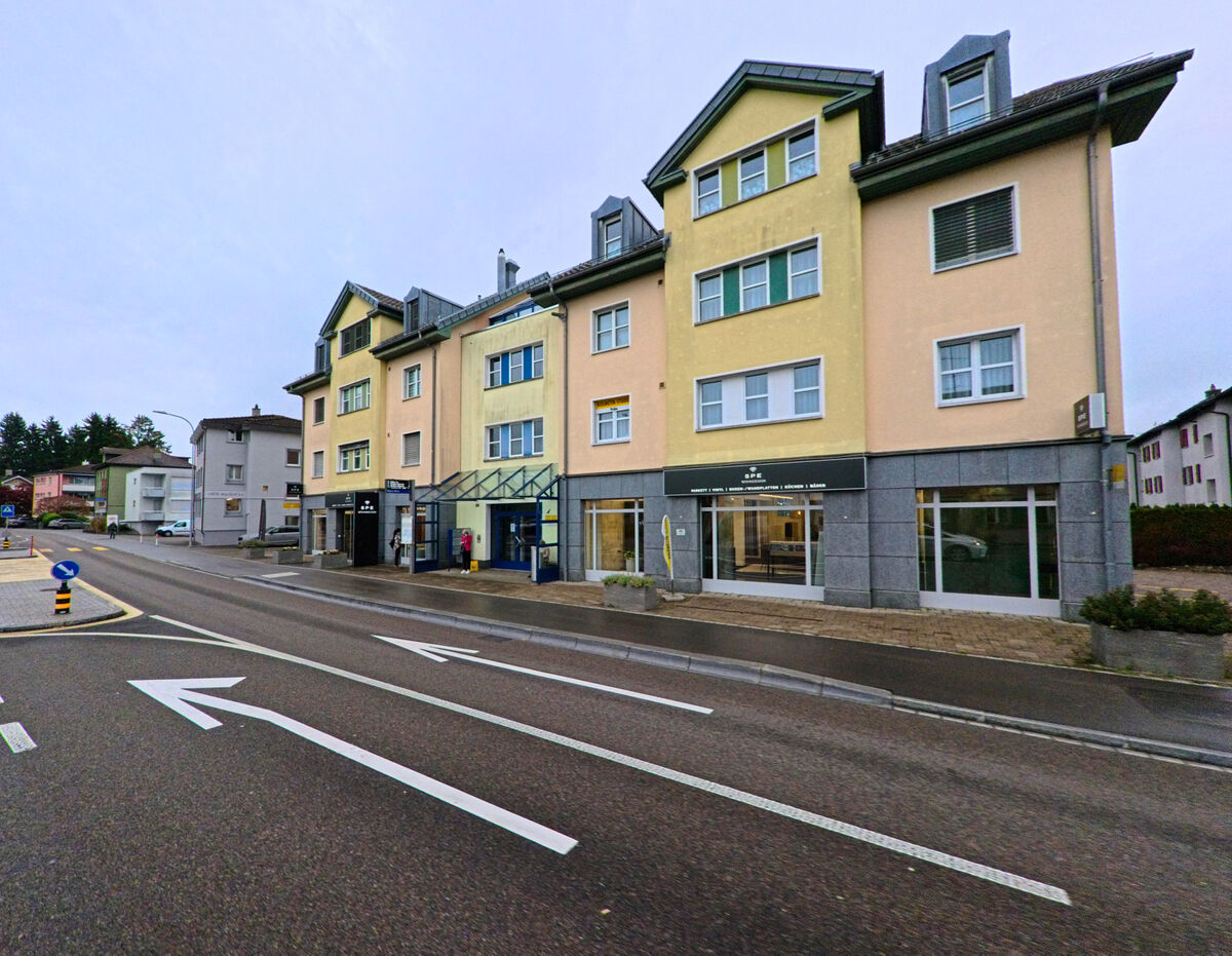 Mehrere Gebaeude mit Laeden im Erdgeschoss reihen sich entlang einer Hauptstrasse in Gossau (9200, Kanton St. Gallen).