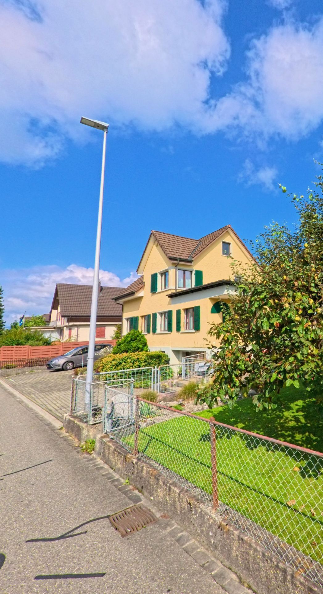 An einer Strassenkurve in Graenichen (5722, Kanton Aargau) stehen moderne Gebaeude mit einer Apotheke und einem Buerohaus unter blauem Himmel.