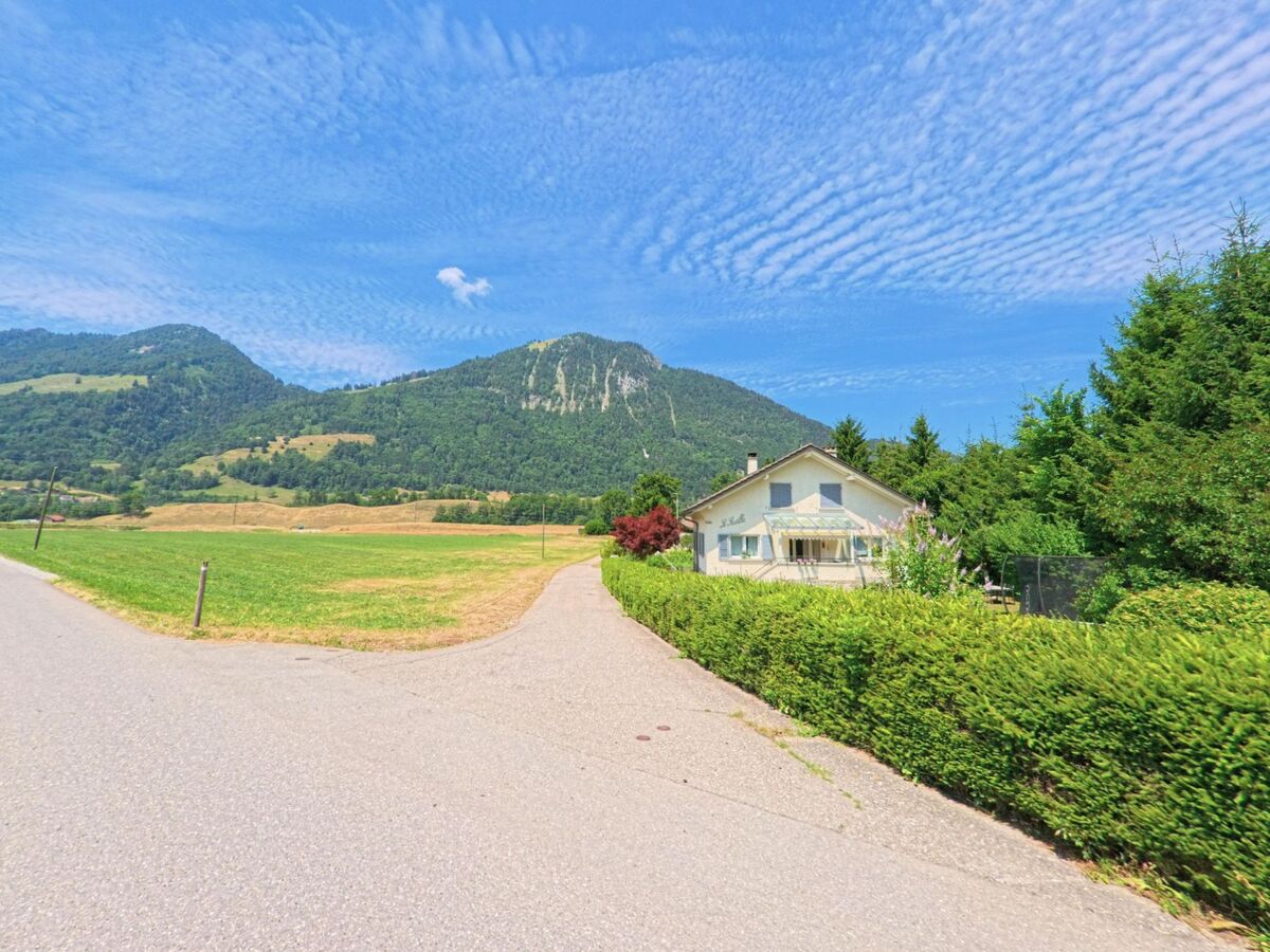 Ein Einfamilienhaus am Waldrand in Grandvillard (1666, Kanton Freiburg) liegt ruhig neben offenen Feldern mit Ausblick auf bewaldete Berghaenge.
