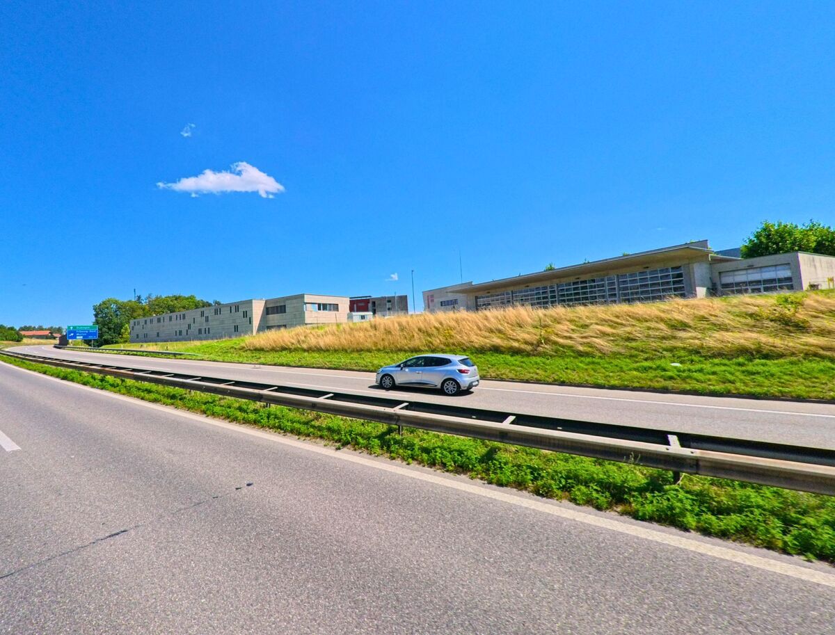 An der Autobahn in Granges-Paccot (1763, Kanton Freiburg) stehen moderne Gewerbe- und Verwaltungsgebaeude hinter einer Boeschung mit trockenem Gras.