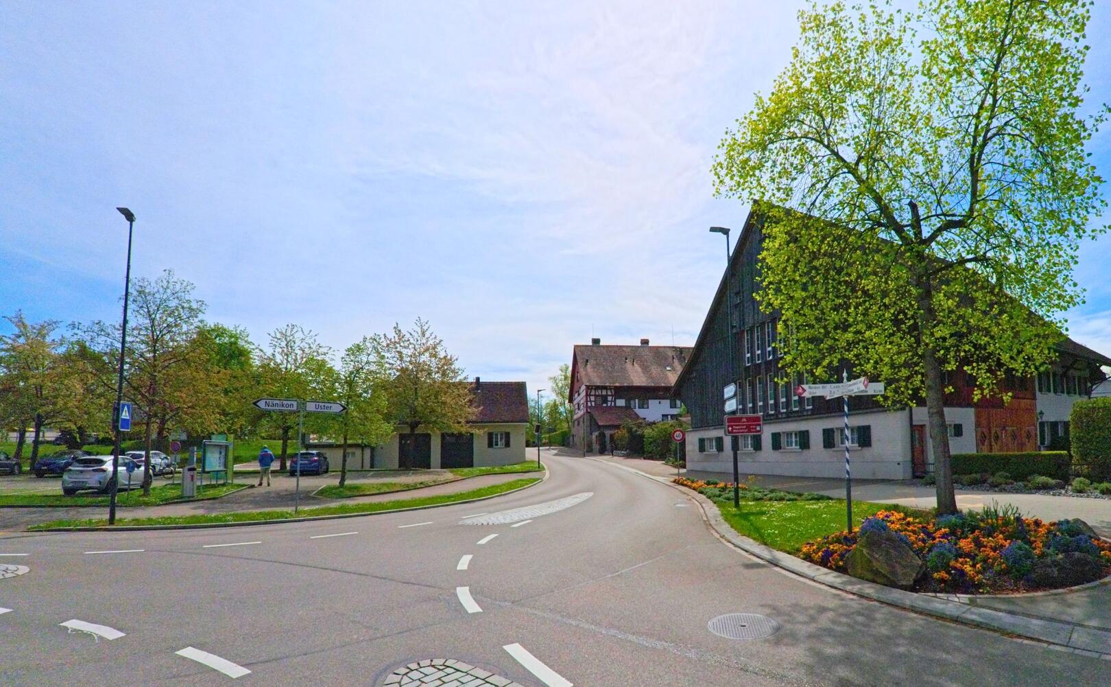 Im ORT Greifensee, PLZ 8606 im KANTON Zürich zeigt das Bild eine verkehrsberuhigte Kreuzung mit historischen Gebäuden und Frühlingsbepflanzung unter klarem Himmel.