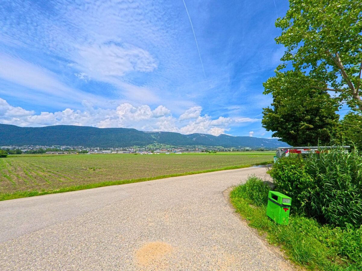 Ein schmaler Weg führt in Grenchen (2540, Kanton Solothurn) an einem weiten Feld entlang mit Blick auf die Stadt und die bewaldeten Hügel des Juras.