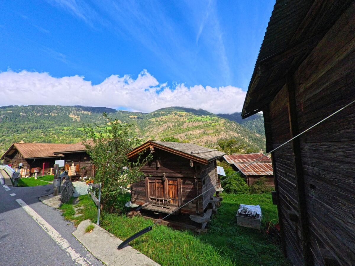Am Strassenrand in Grengiols (3993, Kanton Wallis) stehen kleine traditionelle Speicher aus Holz vor der Kulisse bewaldeter Berghänge.