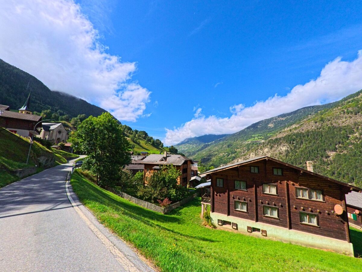 Eine Strasse führt durch Grengiols (3993, Kanton Wallis) vorbei an Holzhäusern und der Kirche, umgeben von den steilen Hängen des Rhonetals.