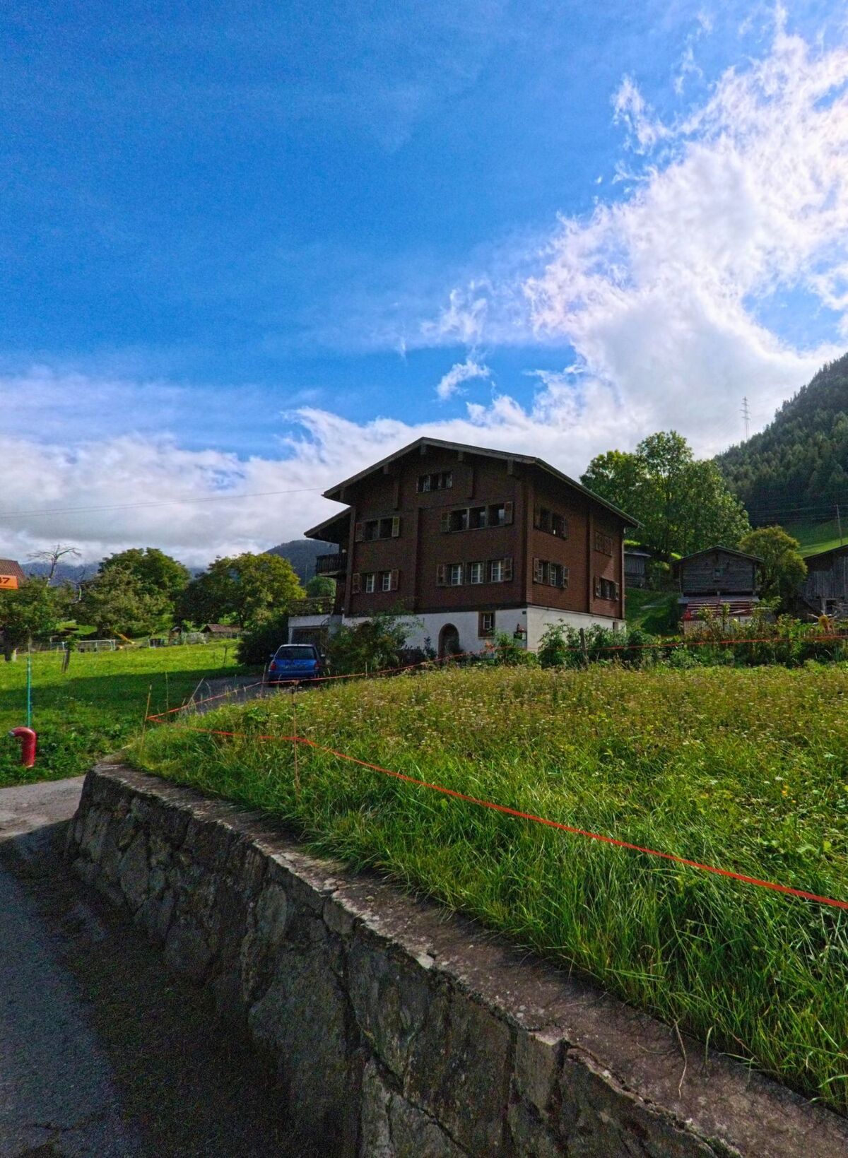 Ein traditionelles Wohnhaus in Grengiols (3993, Kanton Wallis) steht am Rand einer Wiese mit Blick auf die umliegenden Hänge.