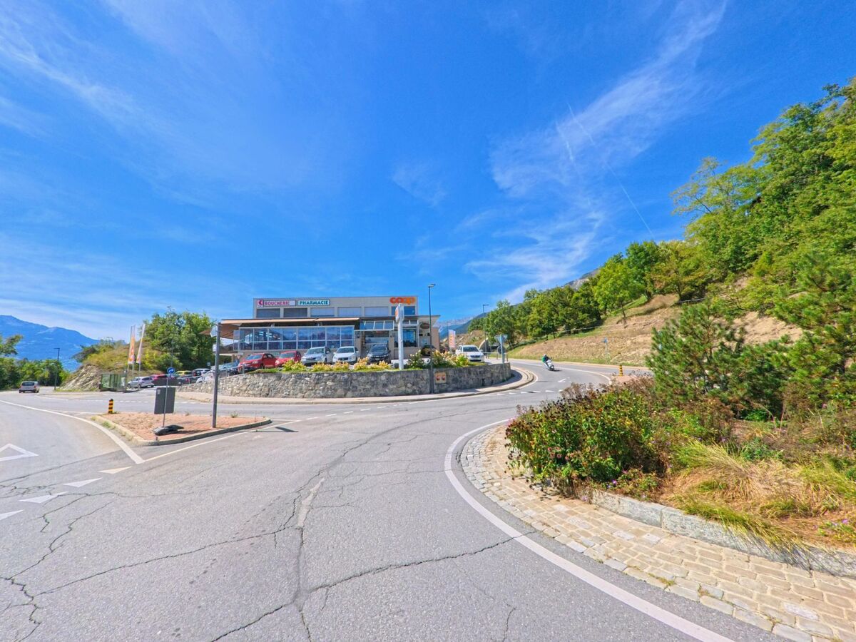 Ein modernes Gebaeude mit Apotheke und Geschaeften steht an einer Strassenkurve in Grimisuat (1971, Kanton Wallis).