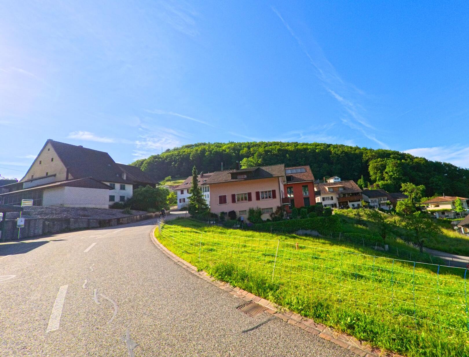 In Grindel (4247, Kanton Solothurn) verläuft eine geschwungene Strasse am Hang entlang, gesäumt von Einfamilienhäusern mit Blick auf bewaldete Höhen.