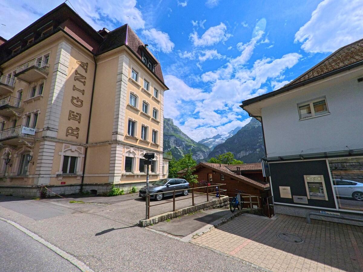 Zwischen einem historischen Hotelgebaeude und einem modernen Geschaeftshaus oeffnet sich in Grindelwald (3818, Kanton Bern) der Blick auf ein Tal mit Gletschern und steilen Bergwaenden.