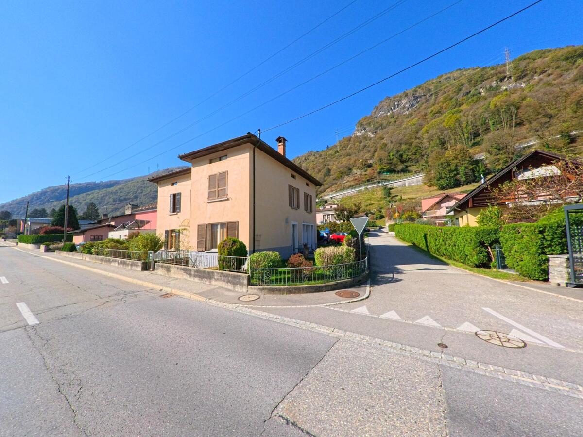 An einer ruhigen Kreuzung in Grono (6537, Kanton Graubünden) steht ein Wohnhaus mit Garten, umgeben von Nebenstrassen und bewaldeten Hängen.