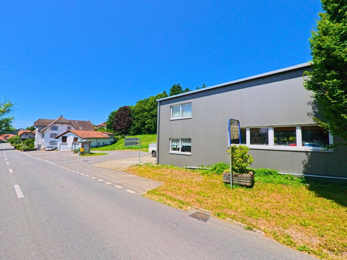 An einer Durchgangsstrasse in Grossaffoltern (3257, Kanton Bern) stehen ein modernes Gewerbegebäude und mehrere Wohnhäuser in direkter Nachbarschaft.