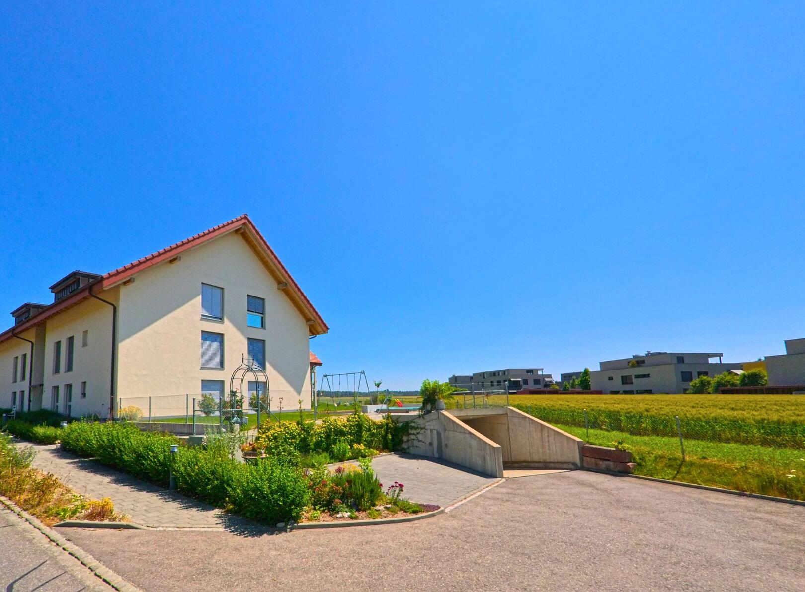 In Grossaffoltern (3257, Kanton Bern) steht ein modernes Wohnhaus mit gepflegtem Garten am Rand eines Neubaugebiets mit Blick auf offene Felder.