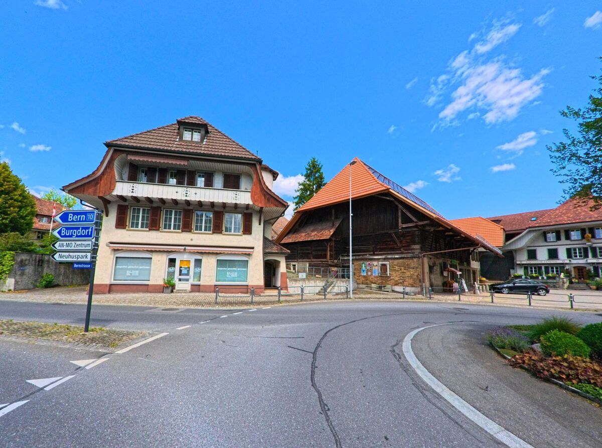 Im Zentrum von Grosshoechstetten (3506, Kanton Bern) treffen sich an einer markanten Kurve historische Wohn- und Wirtschaftsbauten, flankiert von Wegweisern in Richtung Bern und Burgdorf.