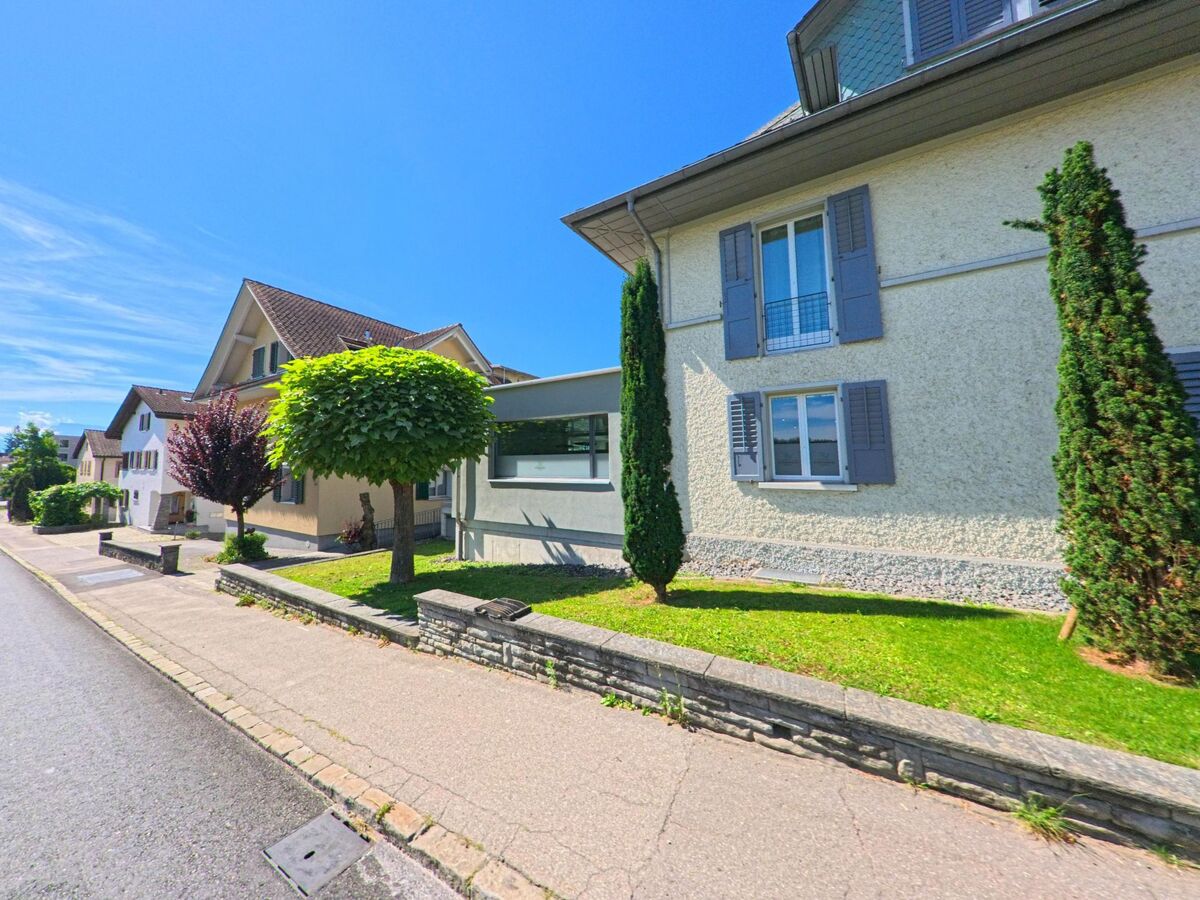 In Grosswangen (6022, Kanton Luzern) stehen mehrere gepflegte Wohnhaeuser mit grauen Fensterlaeden entlang eines Gehwegs, gesaeumt von kleinen Baumen und Gruenflaechen.