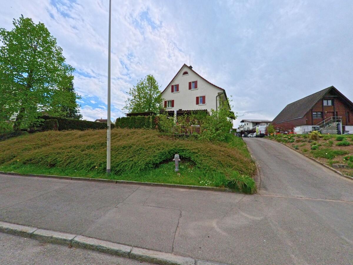 In Grüningen, PLZ 8627 im KANTON Zürich erhebt sich ein Einfamilienhaus mit gepflegtem Garten auf einer leichten Anhöhe neben einem kleinen Privatweg.