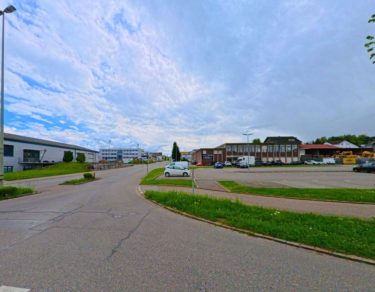 Im Gewerbegebiet von Grüningen, PLZ 8627 im KANTON Zürich säumen moderne Industrie- und Verwaltungsgebäude eine breite Erschliessungsstrasse mit Parkflächen.