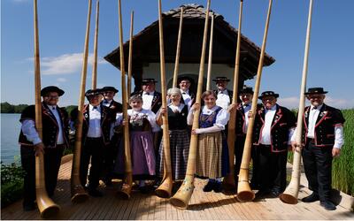 Mitglieder der Alphorngruppe Dagmersellen stehen in traditioneller Tracht mit ihren Alphörnern vor einer Kapelle am See. Die Gruppe pflegt das Schweizer Brauchtum und tritt bei Konzerten, Festen und kulturellen Anlässen in Dagmersellen (6252, Kanton Luzern) auf.