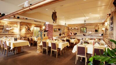 Im Güggeli Sternen in Bözberg ist ein rustikal eingerichtetes Restaurant mit Holzwänden und zahlreichen Hühnerfiguren zu sehen, die auf Regalen, Lampen und Dekoelementen platziert sind, während gedeckte Tische mit gelben Tischdecken einladend wirken.